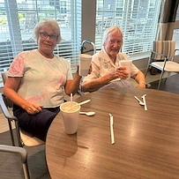 Two residents at Charter Senior Living of Hopkinsville in Hopkinsville, KY, smiling and enjoying root beer floats in the bright dining room with natural light from large windows, highlighting a joyful assisted living and memory care environment.