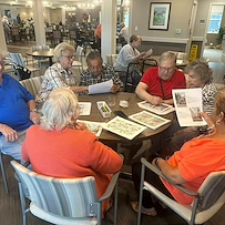 Seniors at Charter Senior Living of Hopkinsville in Hopkinsville, KY, collaborating on a group activity around a wooden table, engaging their minds in assisted living and memory care.