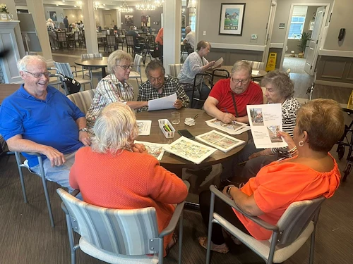 Seniors at Charter Senior Living of Hopkinsville in Hopkinsville, KY, collaborating on a group activity around a wooden table, engaging their minds in assisted living and memory care.