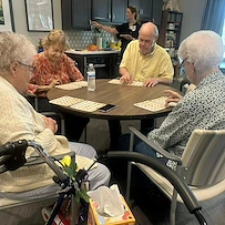 Seniors at Charter Senior Living of Hopkinsville in Hopkinsville, KY, gathered around a common table playing Bingo, fostering social connection in assisted living and memory care.