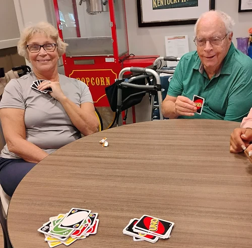Seniors at Charter Senior Living of Hopkinsville in Hopkinsville, KY, sitting around a table playing UNO and smiling, promoting mental engagement and social interaction in assisted living and memory care.